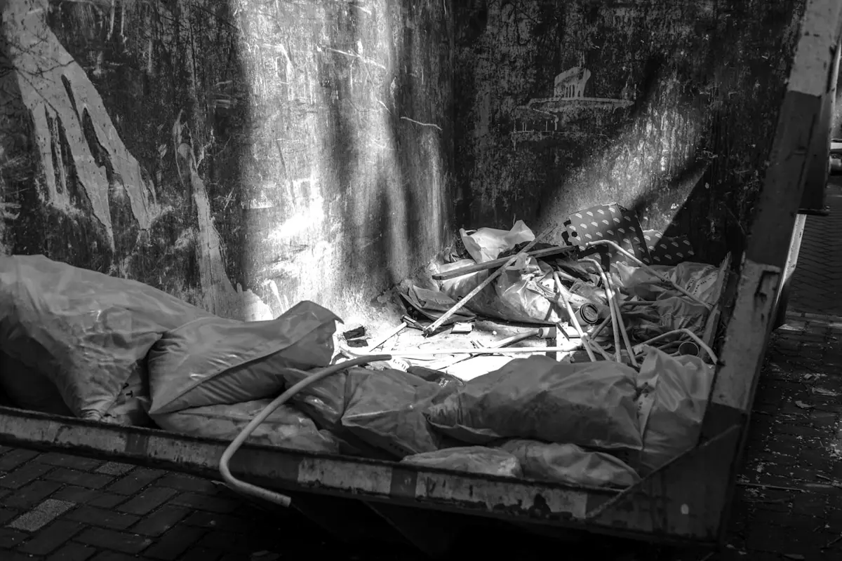 Looking down into a roll-off dumpster holding stuffed trash bags, scrap boards, and pipes.